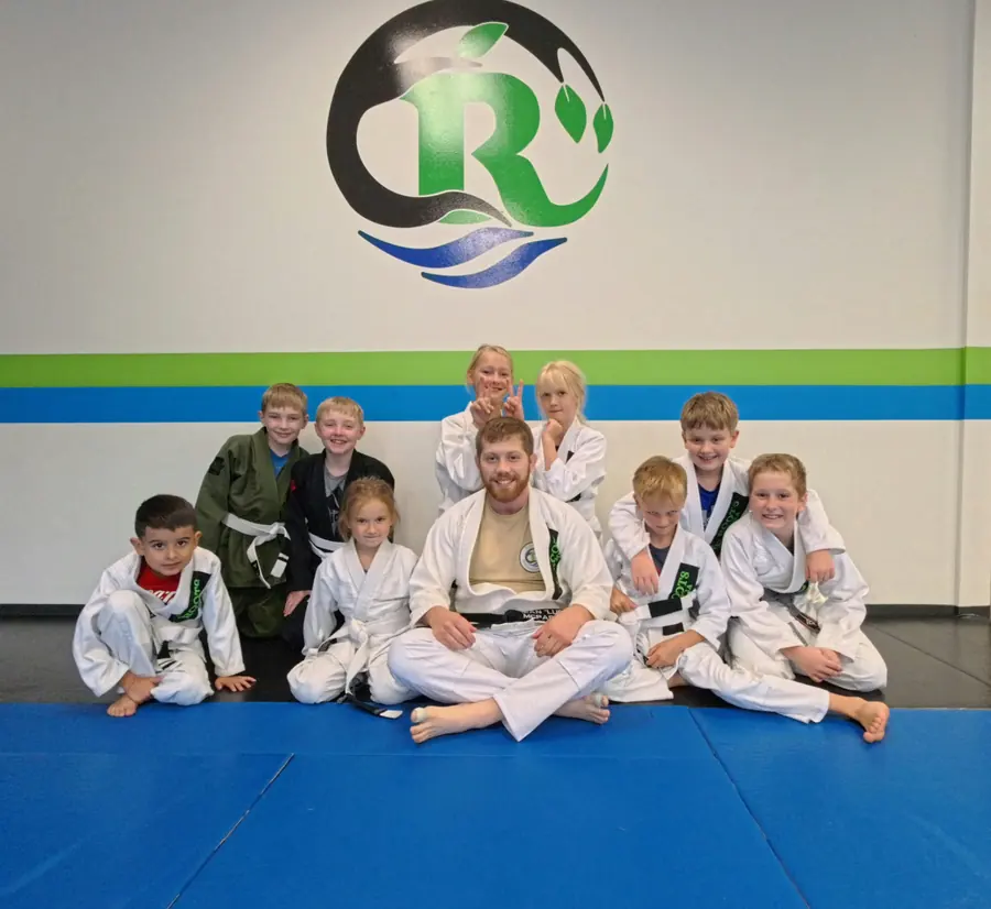 A Roots MMA coach seated with young martial arts students beneath the Roots logo.