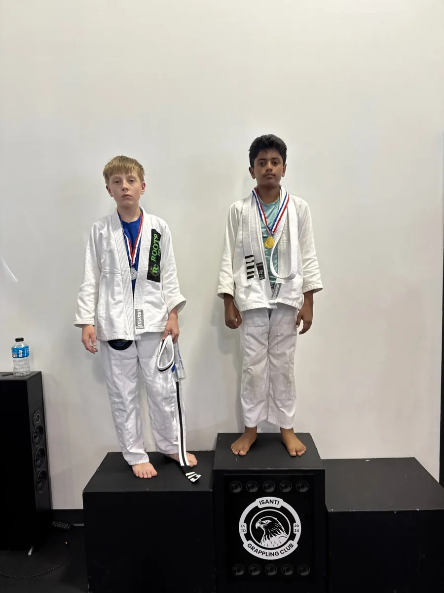 Two teens in martial arts uniforms wearing medals on the tournament podium.